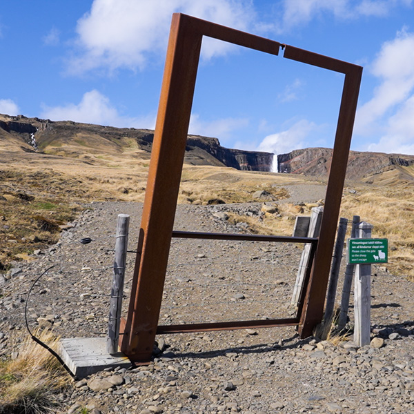 Hikers on rocky trail with view toward Hengifoss waterfall in East Iceland