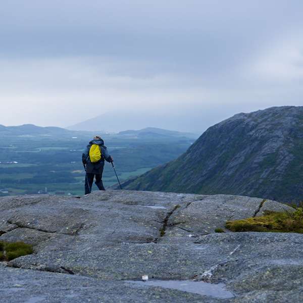Hiker standing on the bare rock summit of Vettfjellet looking out over Sandnessjøen and the coast, Norway