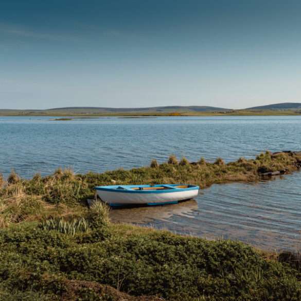 Small blue rowing boat moored in a shallow inlet on the Orkney shore, Scotland