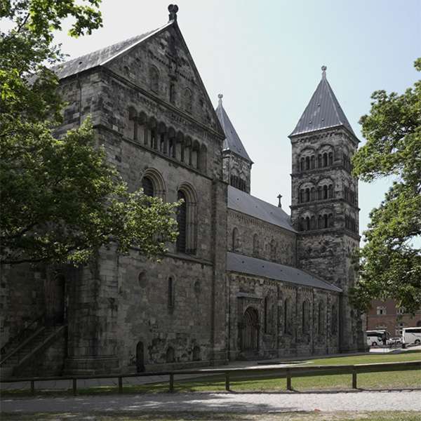 The grey sandstone flank and apse of Lund Cathedral framed by trees