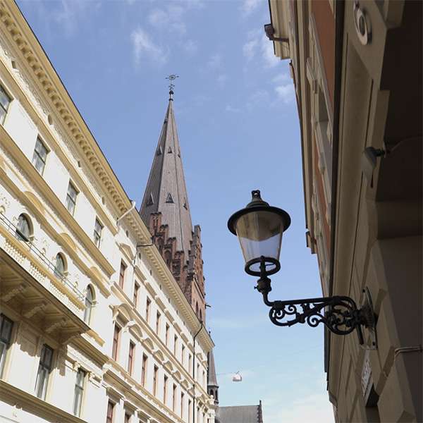 Spire of St Petri church above an old-town street in Malmö, with a wrought-iron street lamp