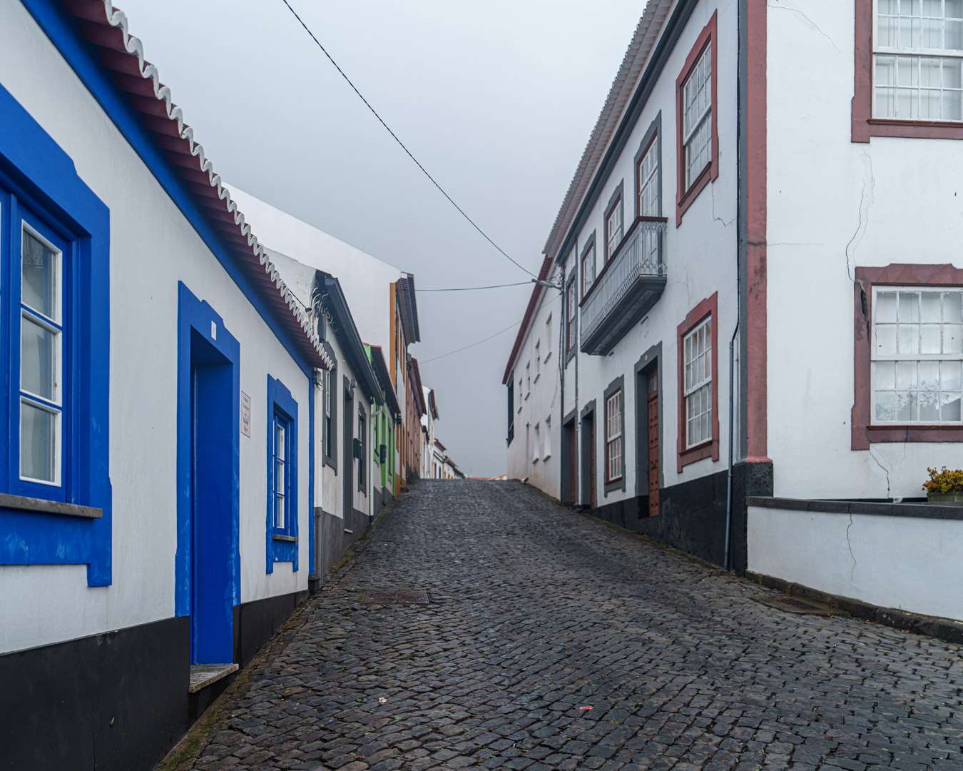 Wet cobbled lane between blue-framed white houses in the old town of Angra