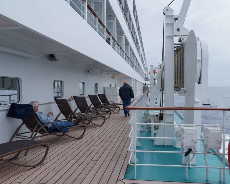 Passengers reading on loungers along the open promenade deck of a cruise ship