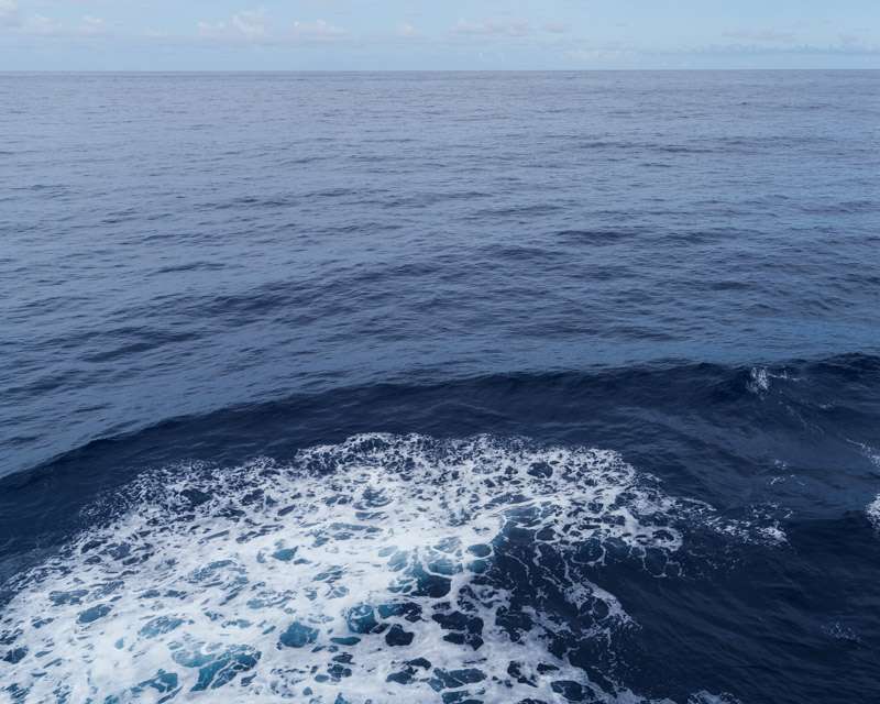The ship's wake breaking white across deep blue open ocean