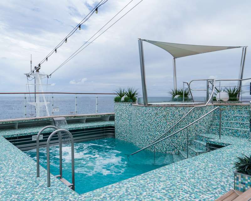 The empty outdoor pool under a white sun sail on a cruise ship deck