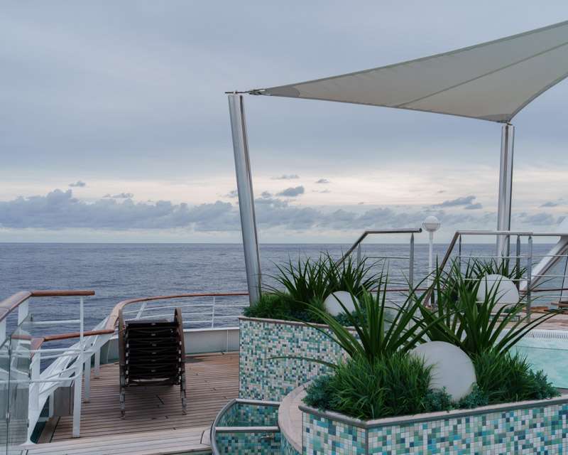 Pool deck with planters and a sun sail looking out over a grey evening sea