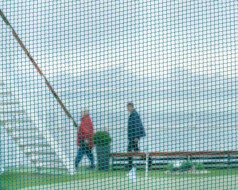 Two passengers walking the deck seen through the green netting of the sports court