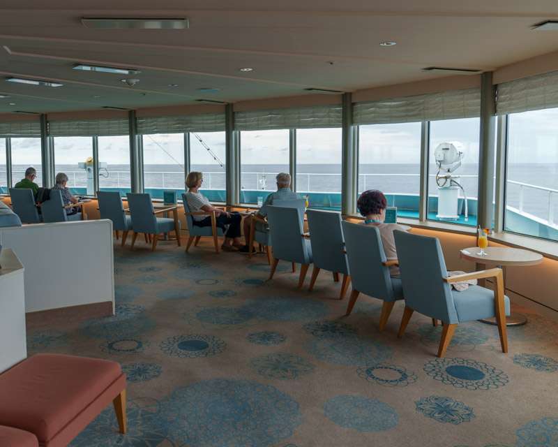 Guests sitting in an observation lounge with panorama windows onto the sea
