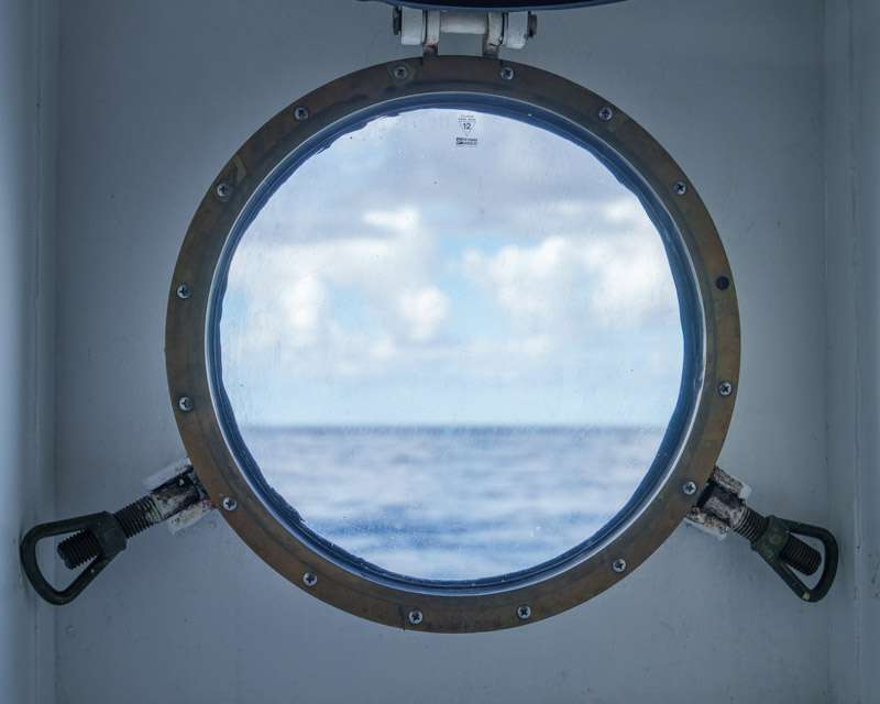 A ship's porthole framing sea and cloud on a day at sea