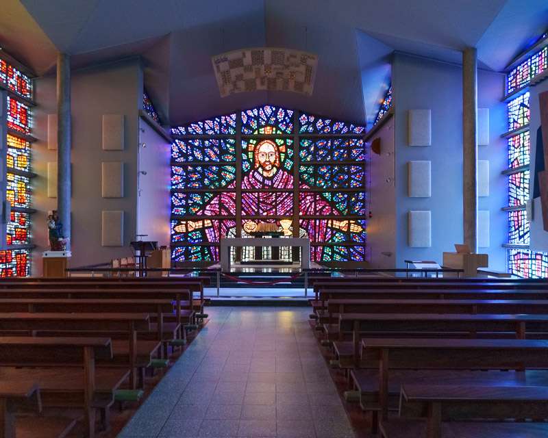 Tall stained-glass window above the altar at Buckfast Abbey, seen down the aisle