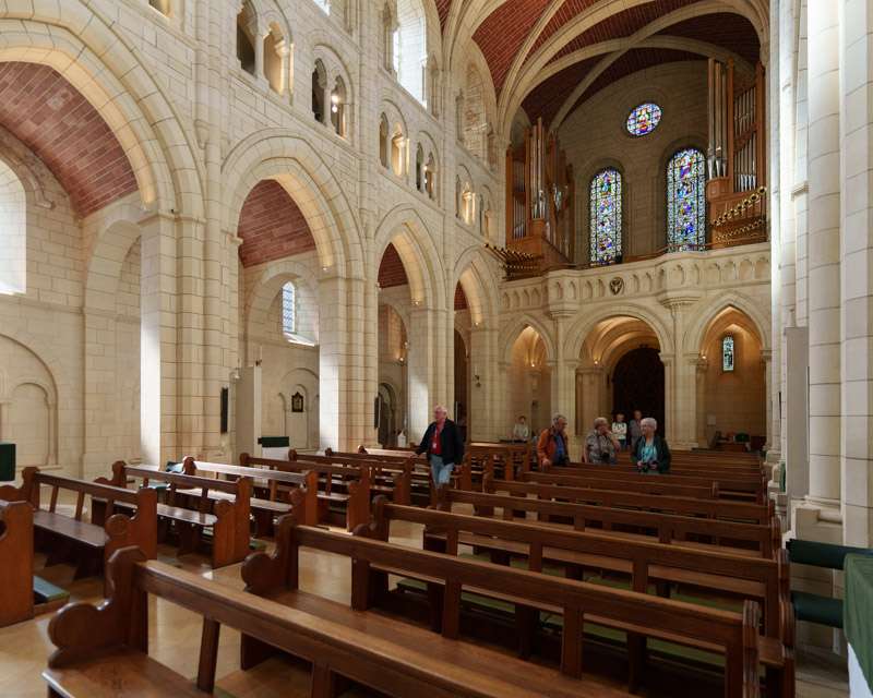 Nave of Buckfast Abbey church with rounded arches and pale stone, wooden pews below