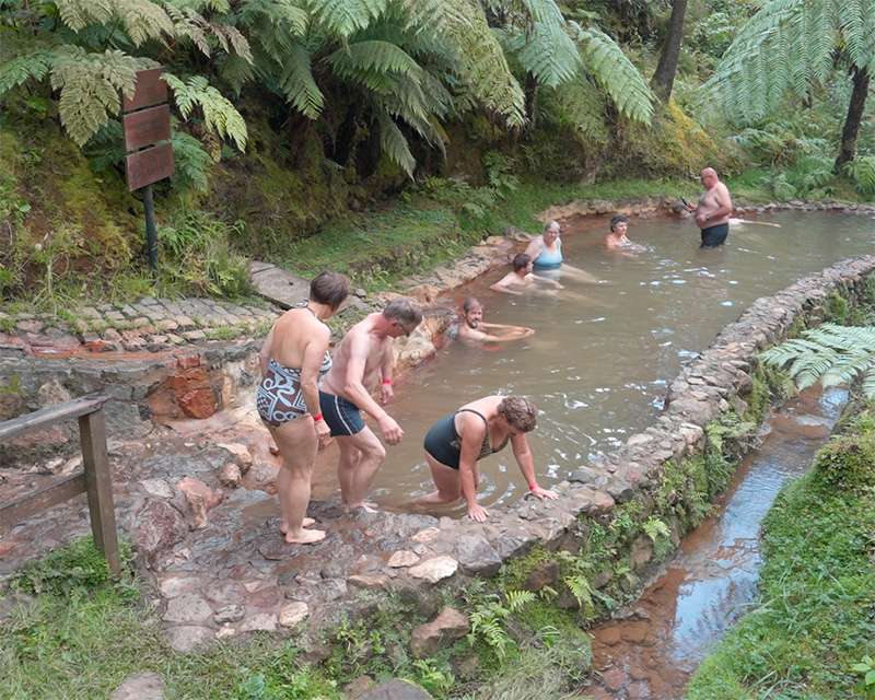 Bathers stepping into the warm iron-brown stream at Caldeira Velha between tall tree ferns, São Miguel
