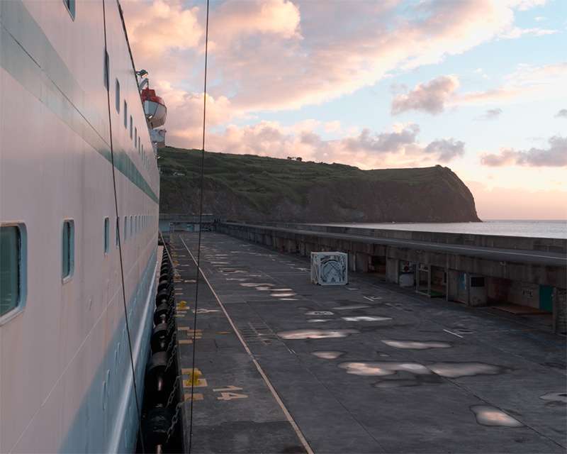 View along the ship's side to the quay and the headland at Horta in the early morning