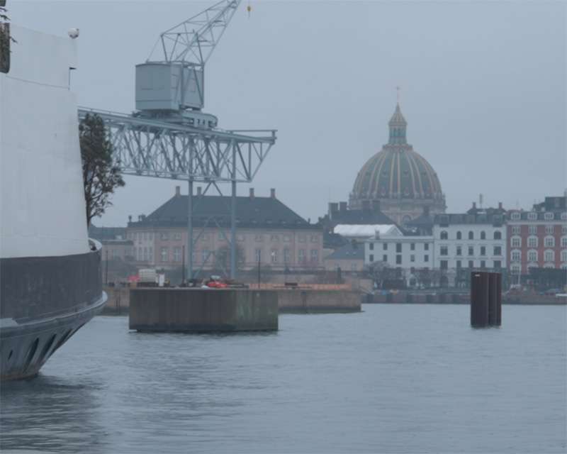 A harbour crane and a green copper church dome in morning haze over Copenhagen