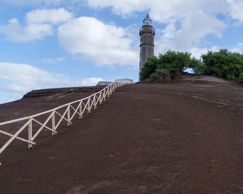 The Capelinhos lighthouse on its ash ridge with the fenced path leading up to it