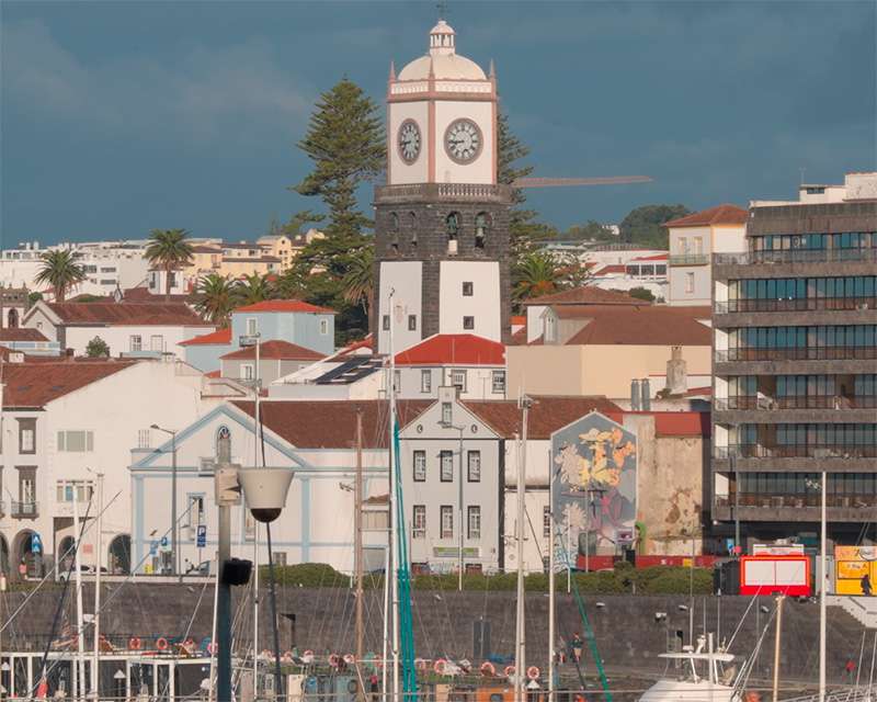 The waterfront of Ponta Delgada seen from the water, church tower with a clock above the white town