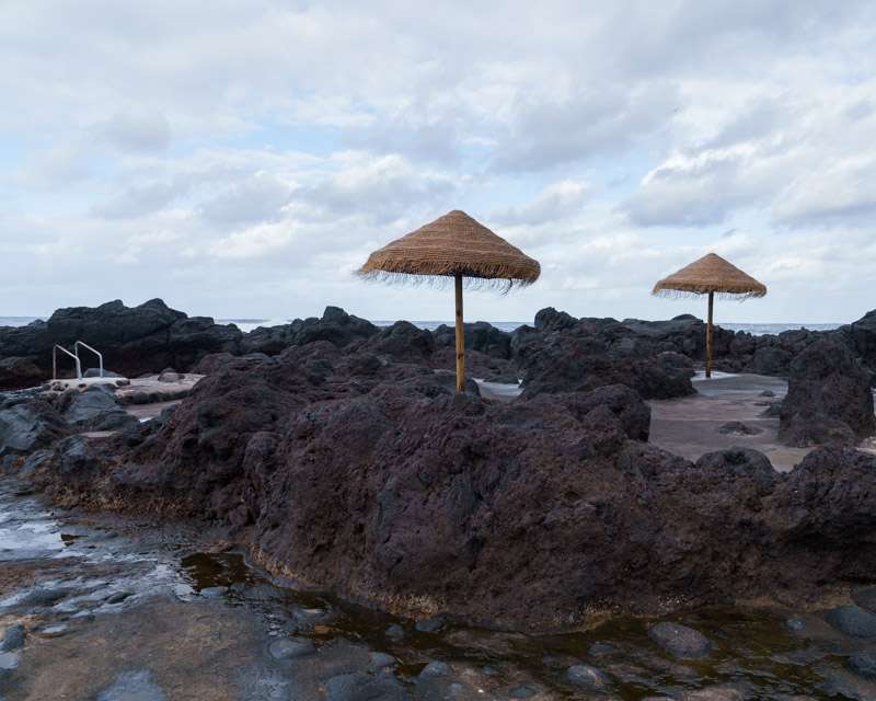 Thatched sun umbrellas beside the bathing pool cut into the lava at Porto do Comprido