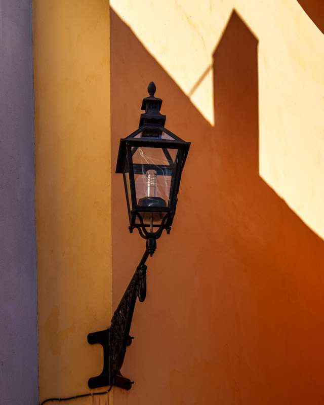 Black wrought-iron street lantern casting a sharp shadow on an ochre wall in Gamla Stan, Stockholm