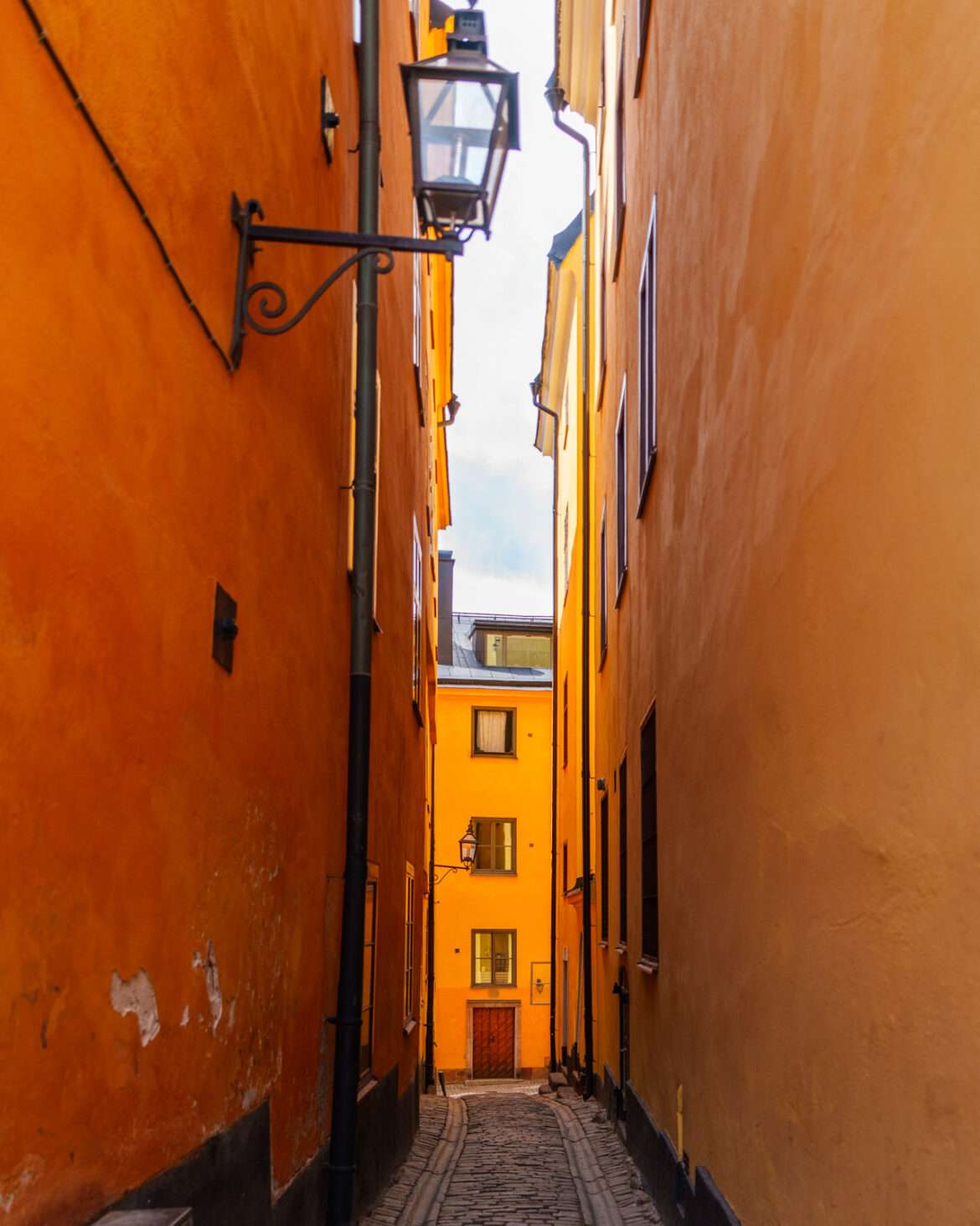 Narrow cobbled alley between ochre facades in Gamla Stan, Stockholm's old town, with a wrought-iron wall lantern