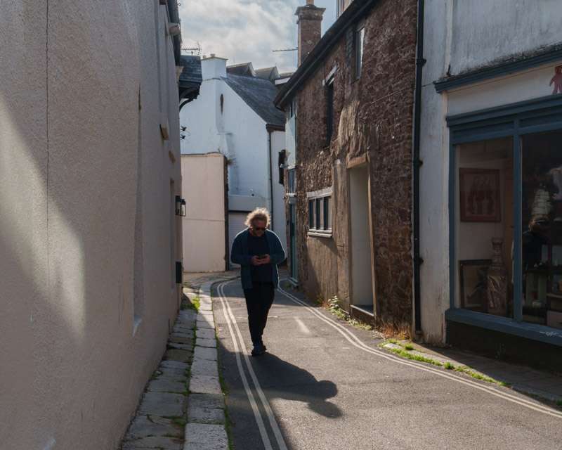 Woman walking up a narrow lane in Totnes in low morning sun, one side of the street in shadow