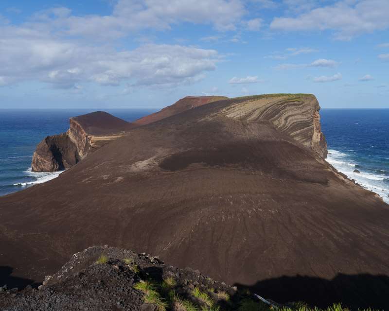 The brown ash cone of Capelinhos falling away to the sea, seen from the coastal trail