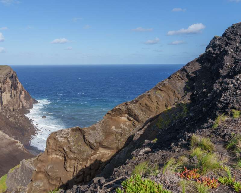 Layered volcanic cliffs above a clear green cove on the Capelinhos coast, Faial