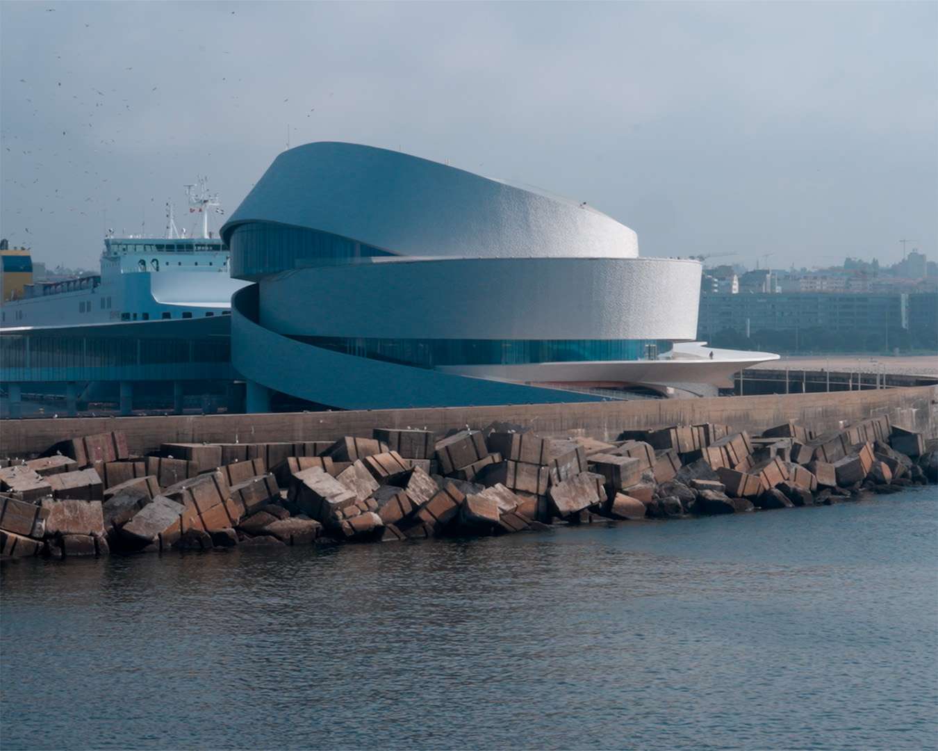 The spiral white cruise terminal of Leix&otilde;es on the breakwater with armour blocks in the foreground