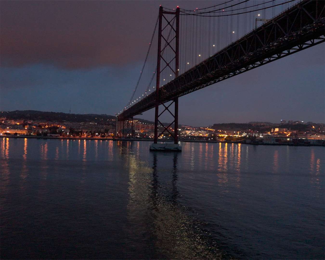 Die beleuchtete Ponte 25 de Abril bei Nacht über dem Tejo bei der Einfahrt nach Lissabon