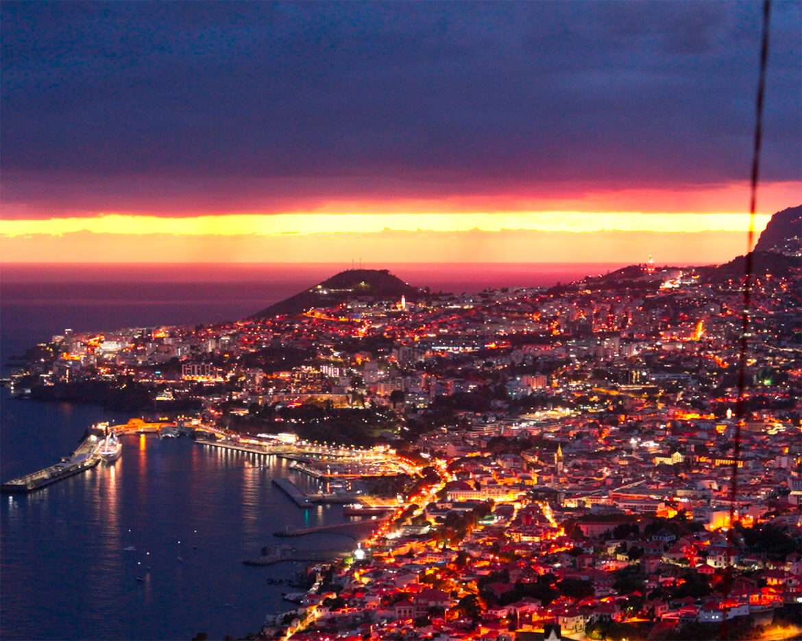 Funchal at sunset from Miradouro do Pinaculo east of the city, bay and city lights below a red sky