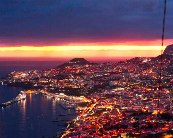 Funchal at sunset from Miradouro do Pinaculo east of the city, bay and city lights below a red sky