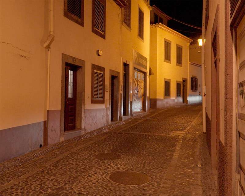 Empty cobbled lane in Funchal old town at night lit by a single street lamp