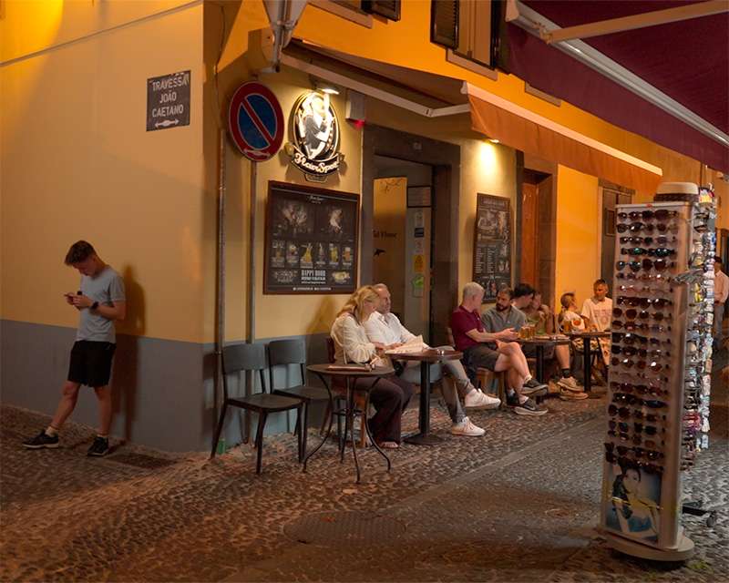 Guests at tables outside a bar on Rua de Santa Maria, Funchal, at dusk