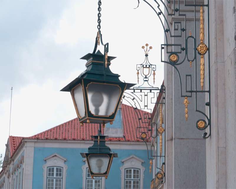 Schmiedeeiserne Laterne vor Ziegeldach und heller Wand des Palasts von Queluz