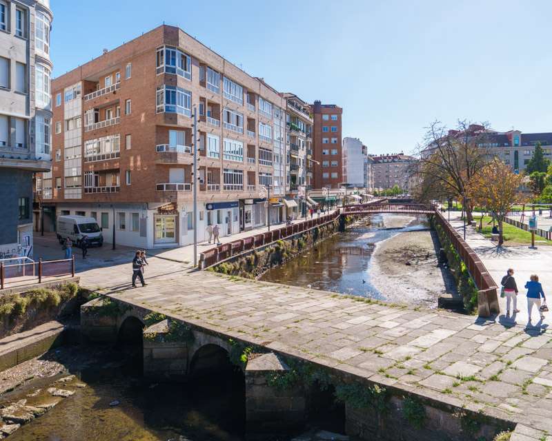 Stone footbridge over the Río Con with the paved riverside walk and apartment blocks, Vilagarcía de Arousa