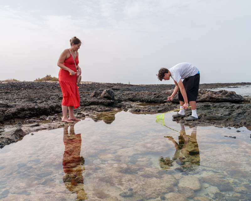 Two people standing in a shallow tide pool on the lava shore at El Cotillo