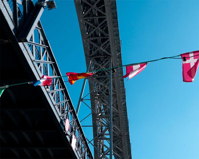 Looking up at the iron lattice of the Lu&iacute;s I bridge past a line of signal flags