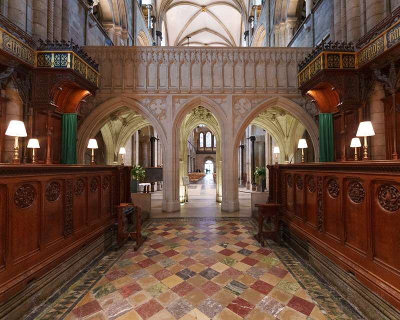The carved choir screen and tiled floor of Chichester Cathedral seen from the nave