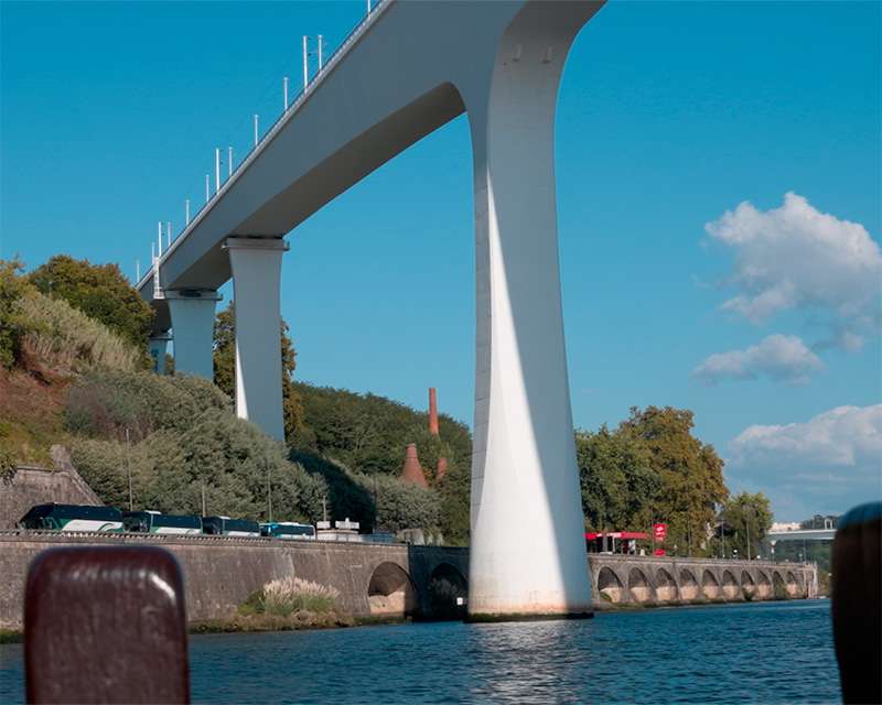 White concrete pier of a modern Douro bridge rising from the water above an old stone arcade