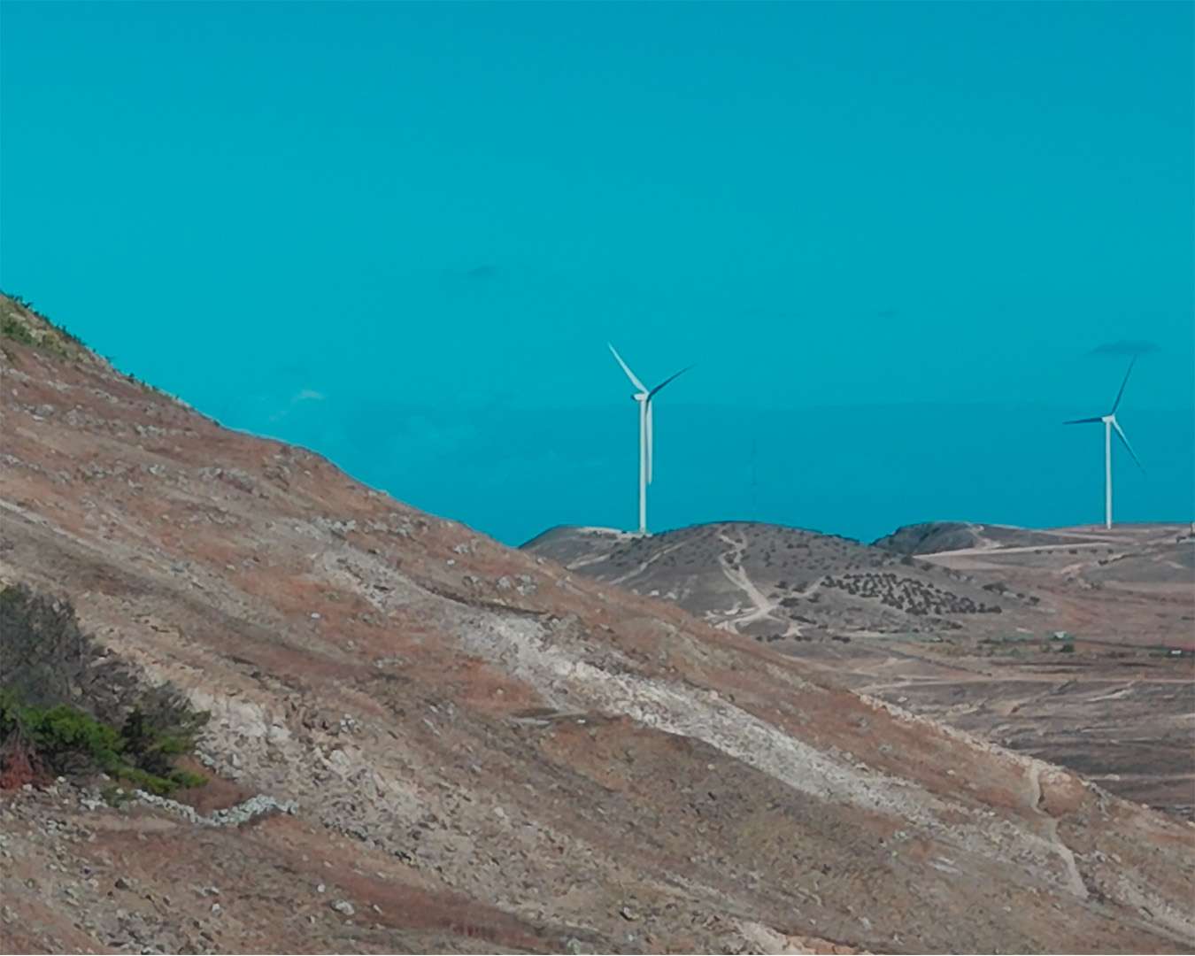 Windräder auf einem kahlen Rücken über dem türkisen Wasser von Porto Santo