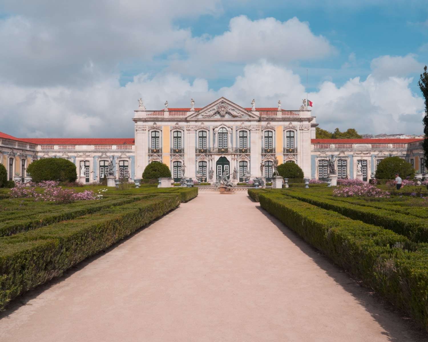 Die Gartenfassade des Palasts von Queluz, gesehen über den Weg zwischen geschnittenen Buchshecken