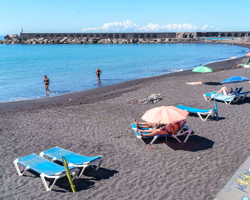 Sunloungers and bathers on the dark sand of Puerto de Tazacorte beach, La Palma
