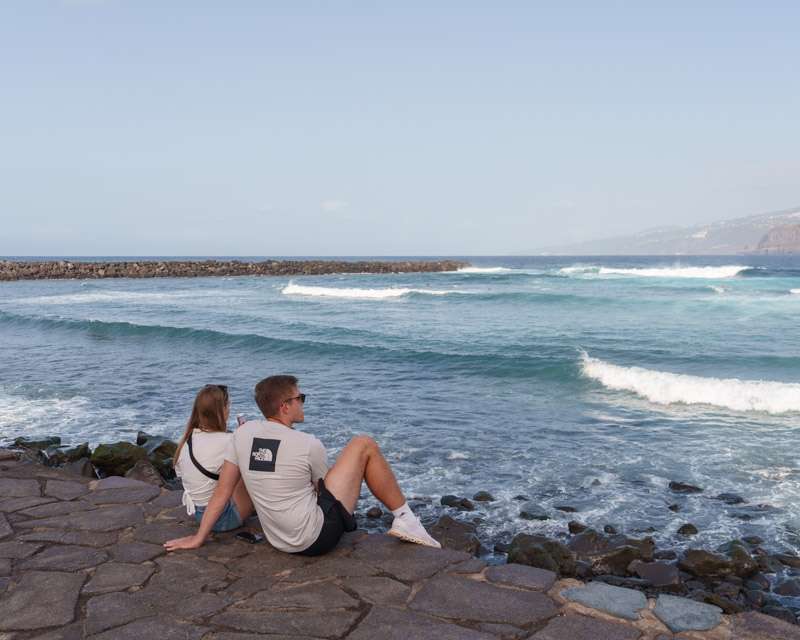 Two people sitting on the sea wall at Puerto de la Cruz while the swell breaks over the rocks