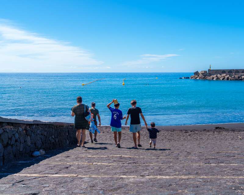 Eine Familie geht am Puerto de Tazacorte zum Wasser, dahinter der Wellenbrecher