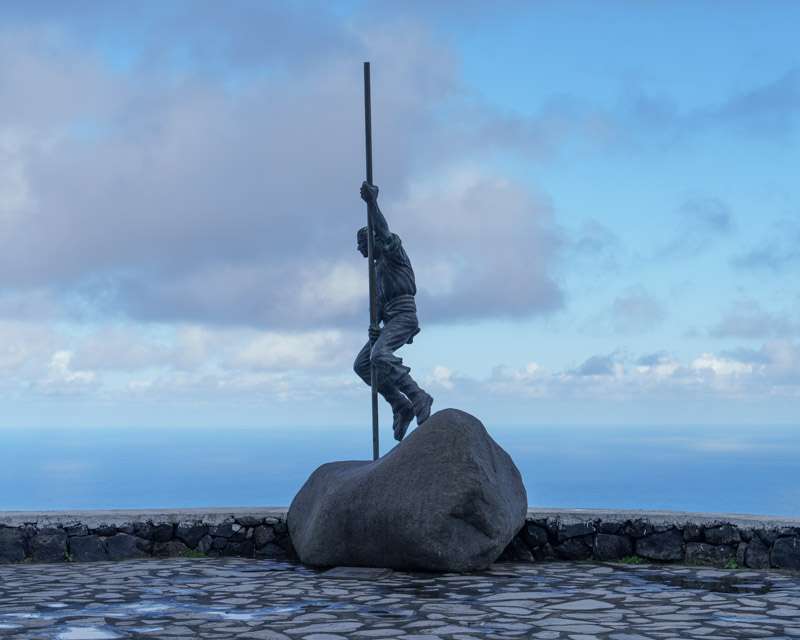 Bronze shepherd with a long jumping pole on a rock at the Mirador de San Bartolomé above the sea