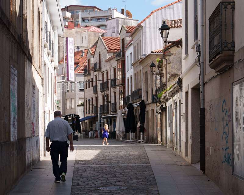 Man walking up the main pedestrian shopping street of Vilagarcía de Arousa past awnings and shops