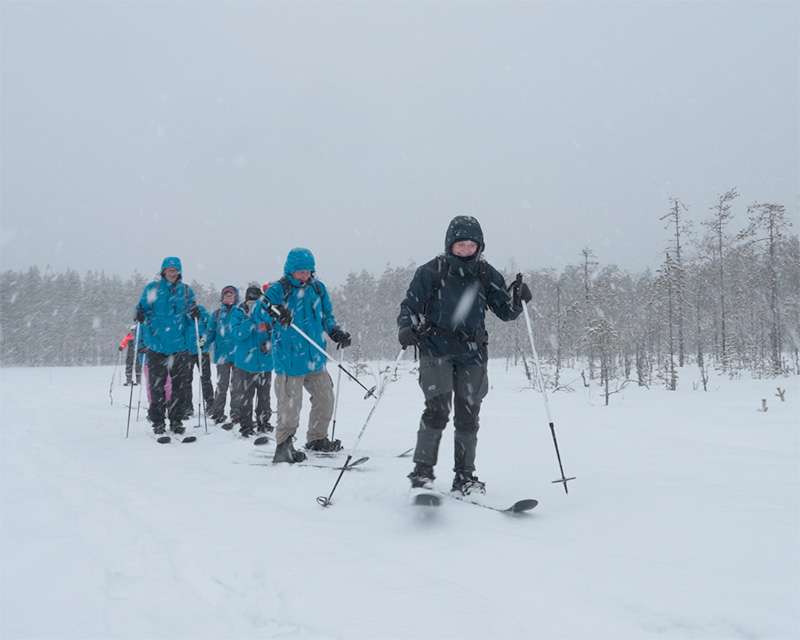 Group crossing the frozen open mire of Pilpasuo on snowshoes in falling snow