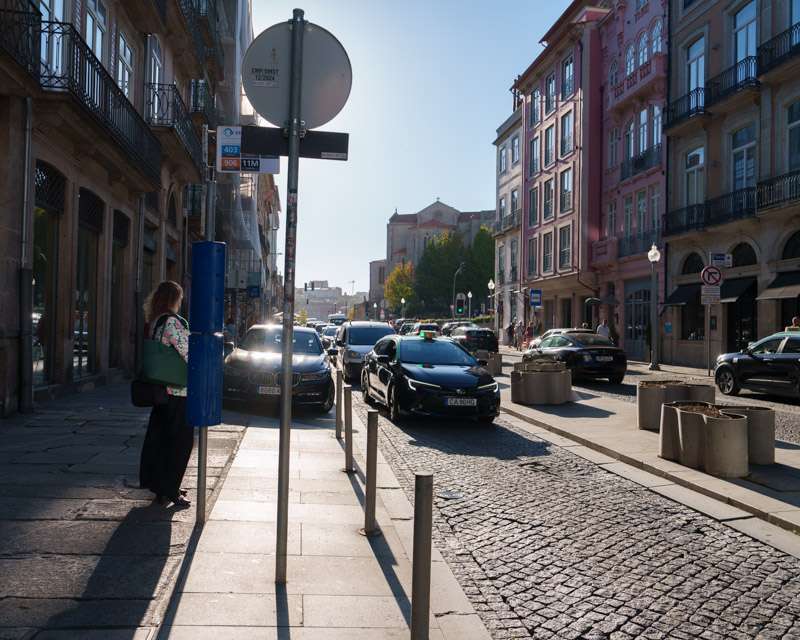 Stra&szlig;enszene in Porto mit Verkehr, Kopfsteinpflaster und einer Frau an der Ampel
