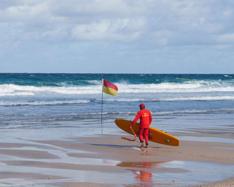 Lifeguard carrying a board past the red and yellow flag on Porthmeor Beach, St Ives