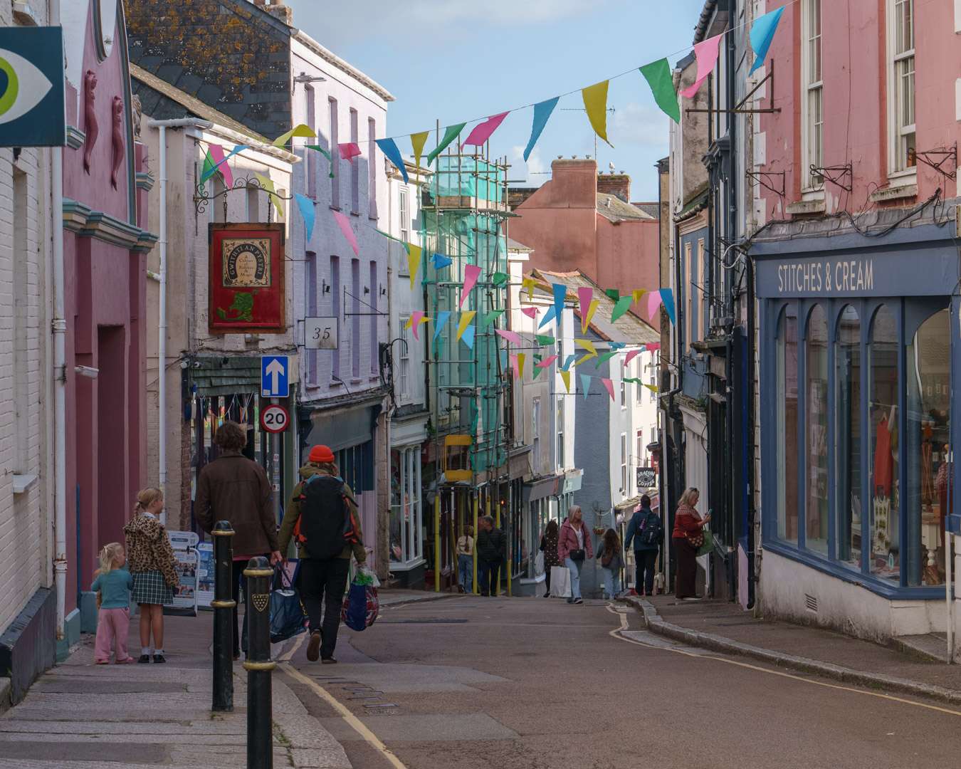 Shoppers in a pastel-painted shopping street in Falmouth old town under rows of bunting