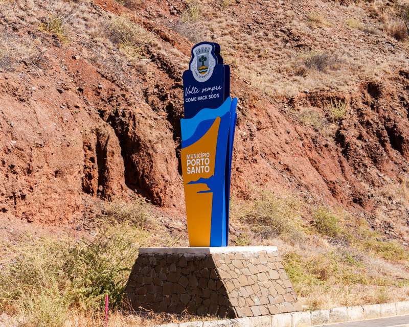 Schild der Gemeinde mit der Aufschrift Volte sempre vor einer roten Felswand auf Porto Santo